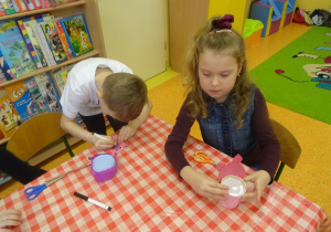 Chłopiec dorysowuje elementy na sylwecie świnki, dziewczynka dokleja elementy papierowe pudełka.